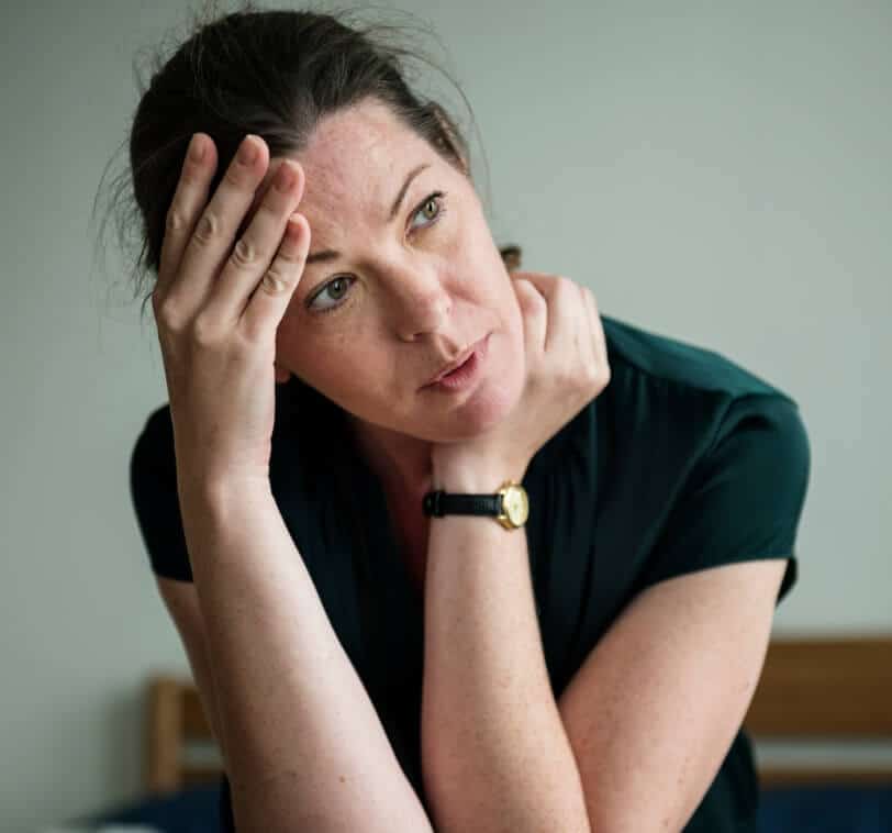 A woman with dark hair holds her head in her hands and looks stressed