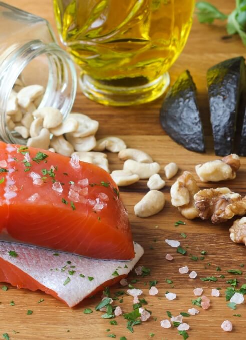 Various antiinflammatory foods, like salmon, nuts, olive oil and avocado on a cutting board