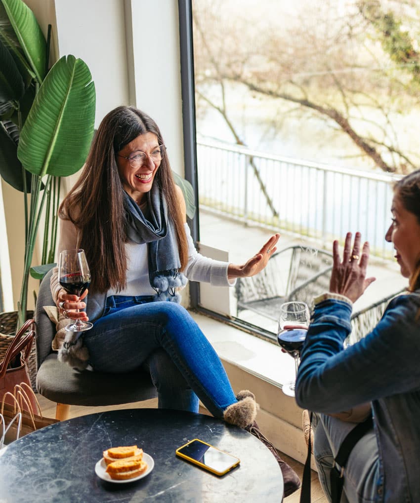 A middle-aged woman has a glass of wine and chats with her friend at a cafe, autoimmune wellness support group