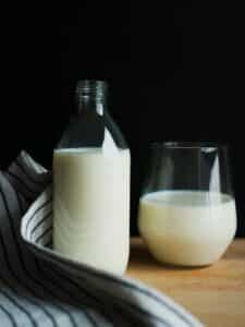 Glass of milk next to bottle of milk on wood table with tablecloth. Dairy swaps for inflammation.