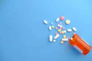 Splattering of colorful pills out of a prescription bottle on a blue background; autoimmune disease treatments
